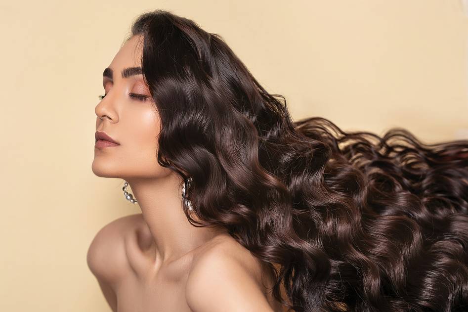A close-up of beautifully textured hair with styling products on a soft pink background